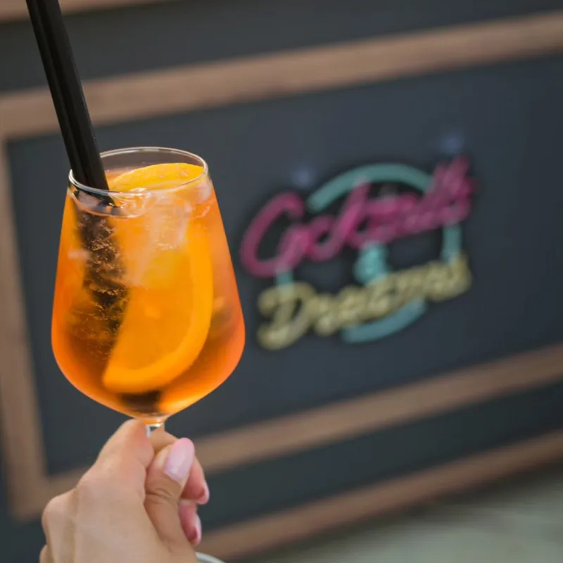 Aperol spritz u ruci ispred neonskog natpisa Cocktails &amp; Dreams